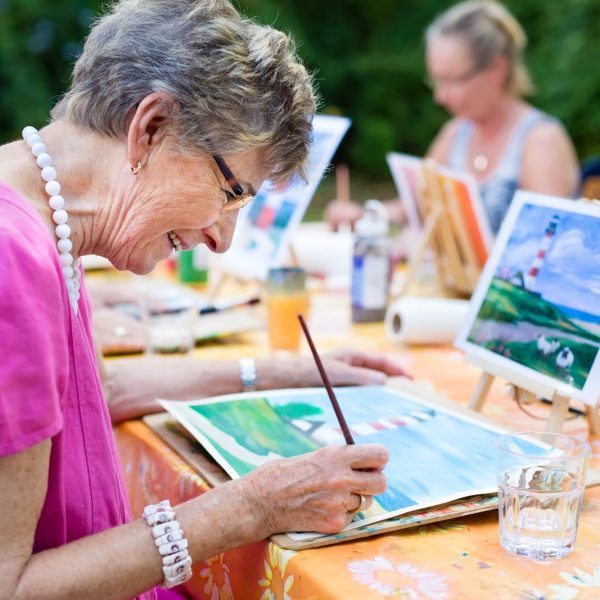 Senior woman smiling while drawing with the group. Side view of a happy senior woman smiling while drawing as a recreational activity or therapy outdoors together with the group of retired women.